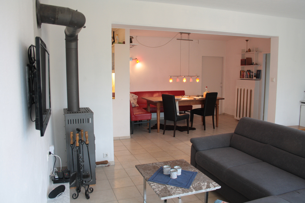 Wohnbereich mit Holzofen und Sofa, Essecke mit Eckbank, großem Tisch und Stühlen